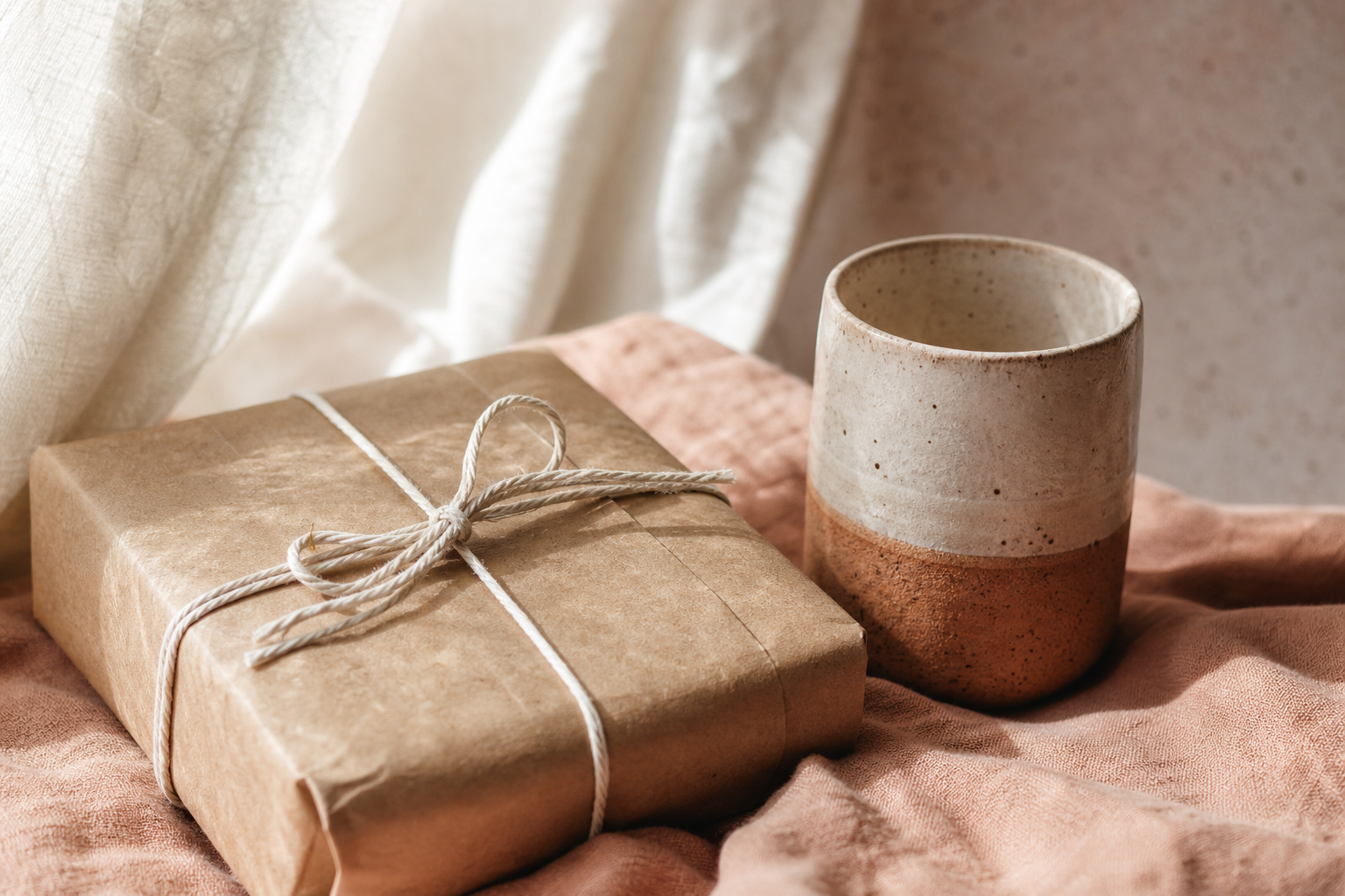 Un paquet en papier kraft noué de ficelle, posé sur un linge en lin avec une tasse en céramique.